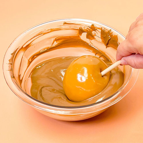 caramel apple being dipped into melted chocolate wafers