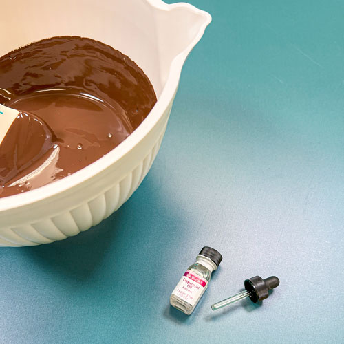 melted dark chocolate wafers in bowl with peppermint oil