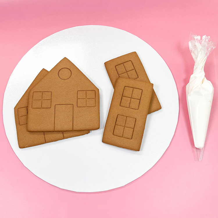 Gingerbread house pieces on a cake board with an icing bag of royal icing