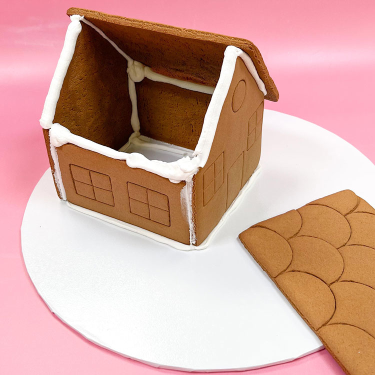 One side of gingerbread house with roof attached. Other side iced for adding other roof piece.