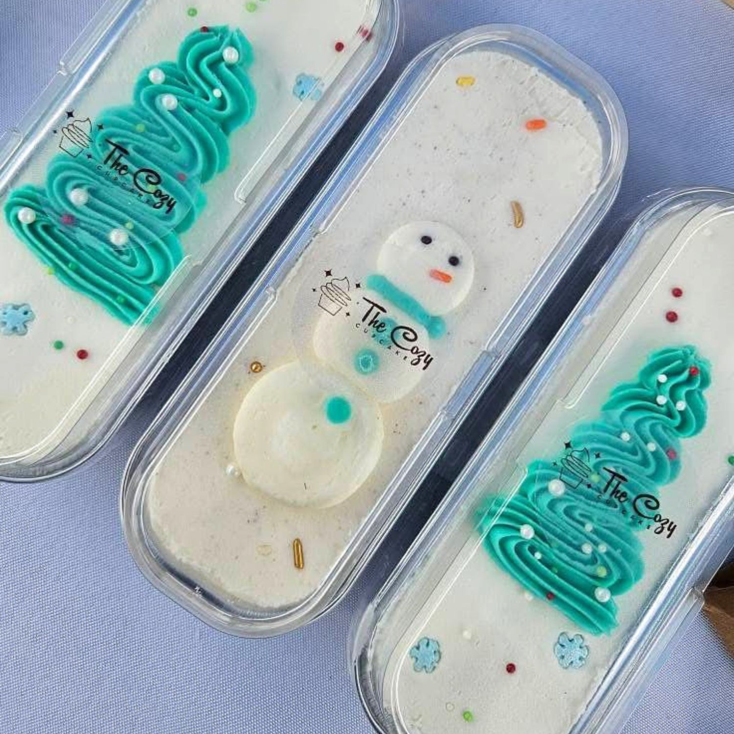 three loaf cakes decorated for winter, snowman and trees in aqua