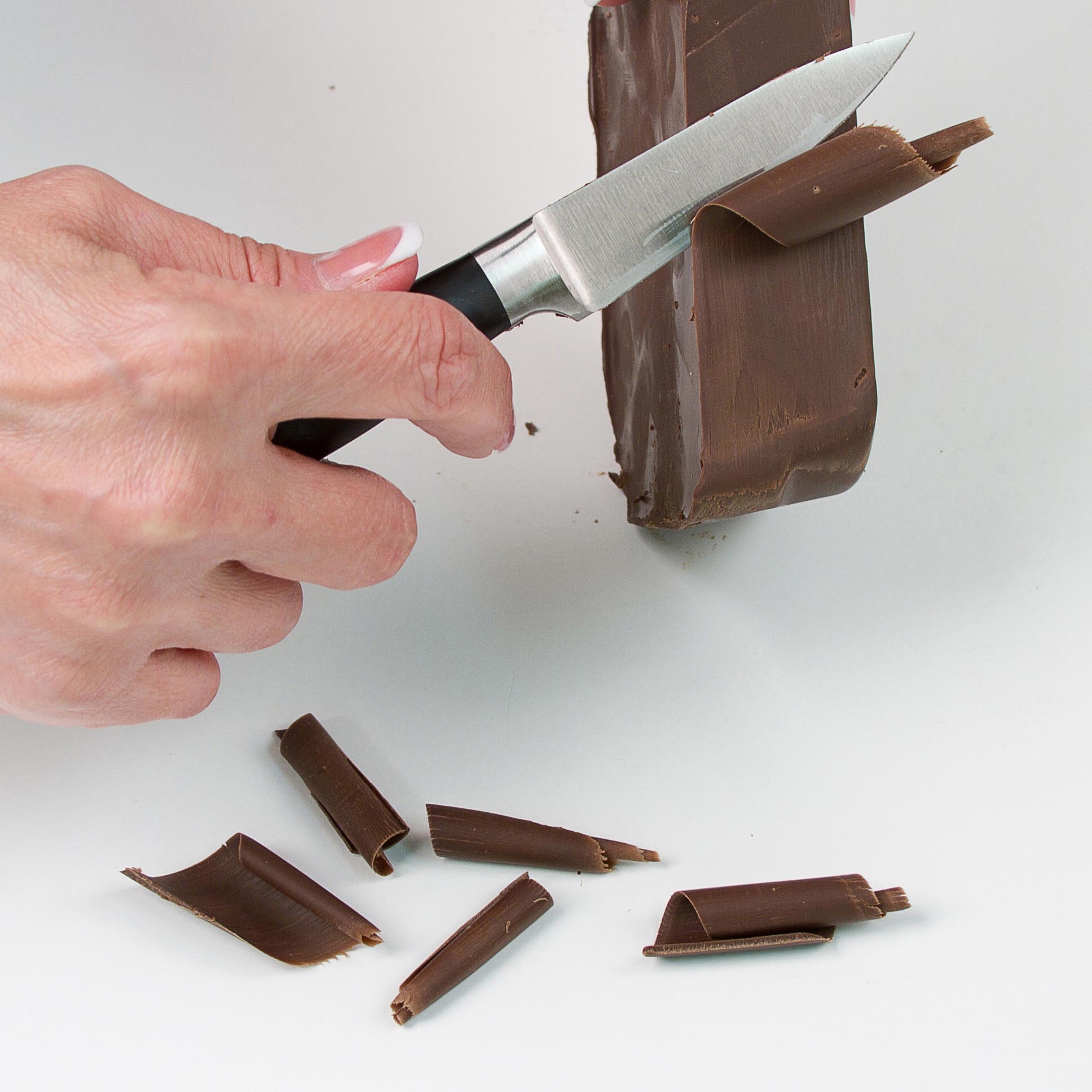 Hold the sharp knife at a slight angle and firmly scrape along the edge of the chocolate block. The chocolate will naturally curl as it shaves away.