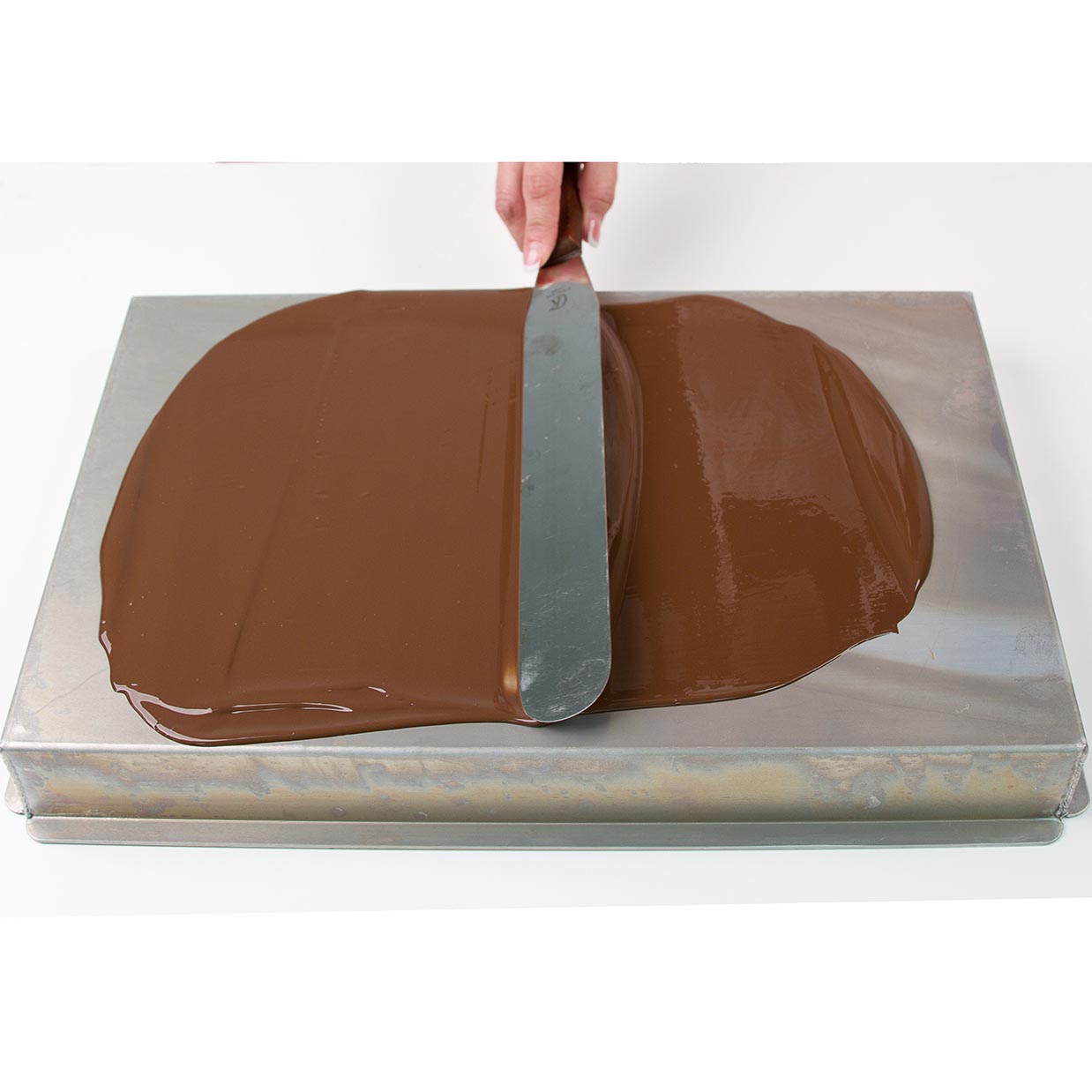 using spatula to spread chocolate on metal baking pan surface