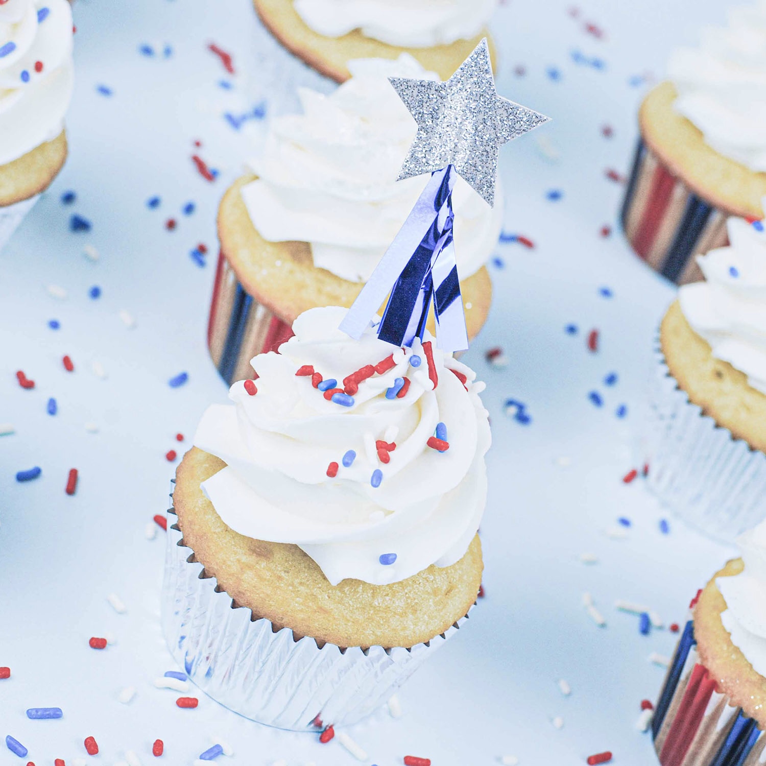 white cake baked in stars and stripe liners with a shooting star pick, dash of red white and blue sprinkles and a spray of sparkle silver dust.