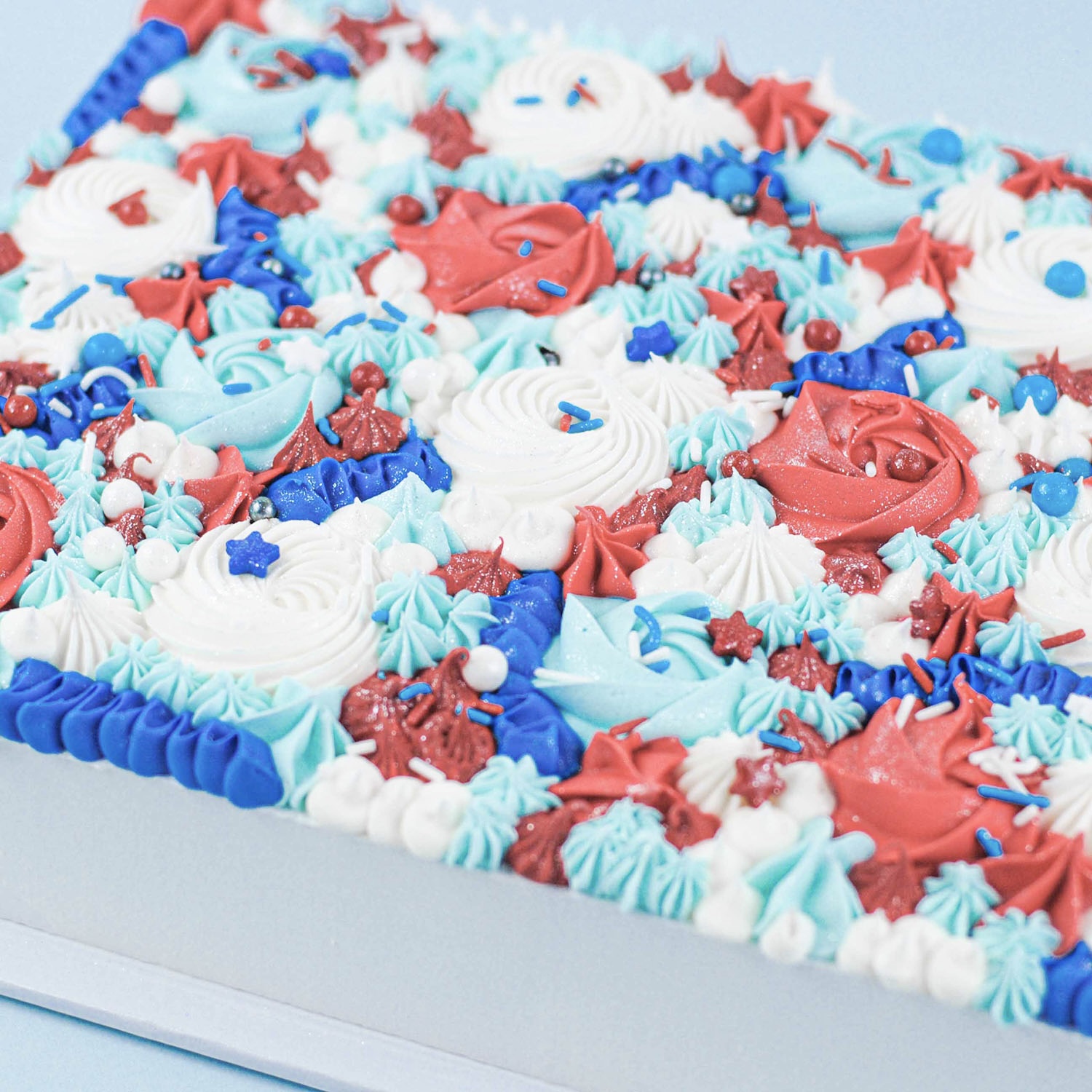 sheet cake decorated in red, white and blue buttercream rosettes, dollops and ribbons and finished with candy pearls, stars and jimmes with a spray of jewel dust.