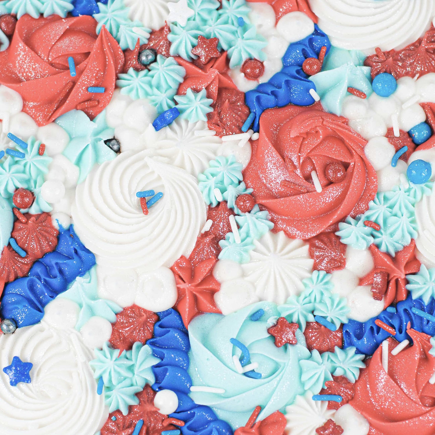 Large white and red buttercream rosettes, light blue and blue star dollops and ribbons in blue and white buttercream with star, pearl and jimmie sprinkles and jewel dust fo sparkle.