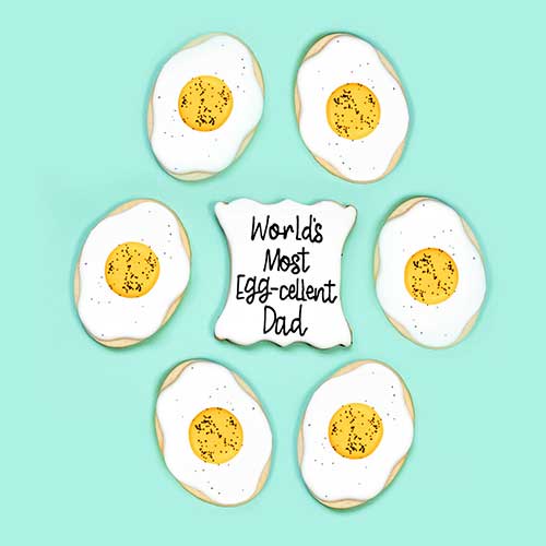 Fried egg cookies decorated in royal icing and a plaque cookie that says World's Most Egg-cellent dad!