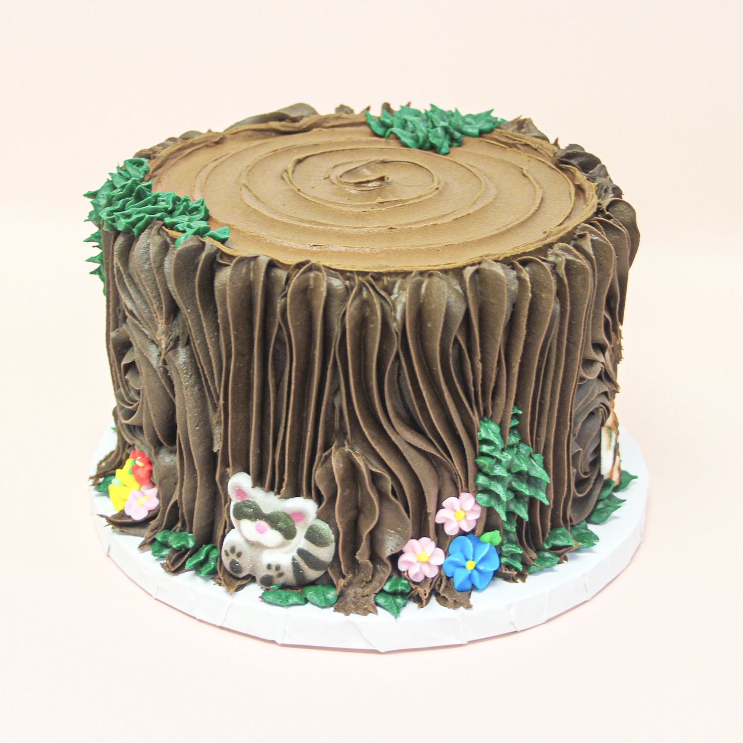Tree stump cake with chocolate buttercream piped bark, green buttercream leaves, icing sugar decorations in flowers and woodland animals.