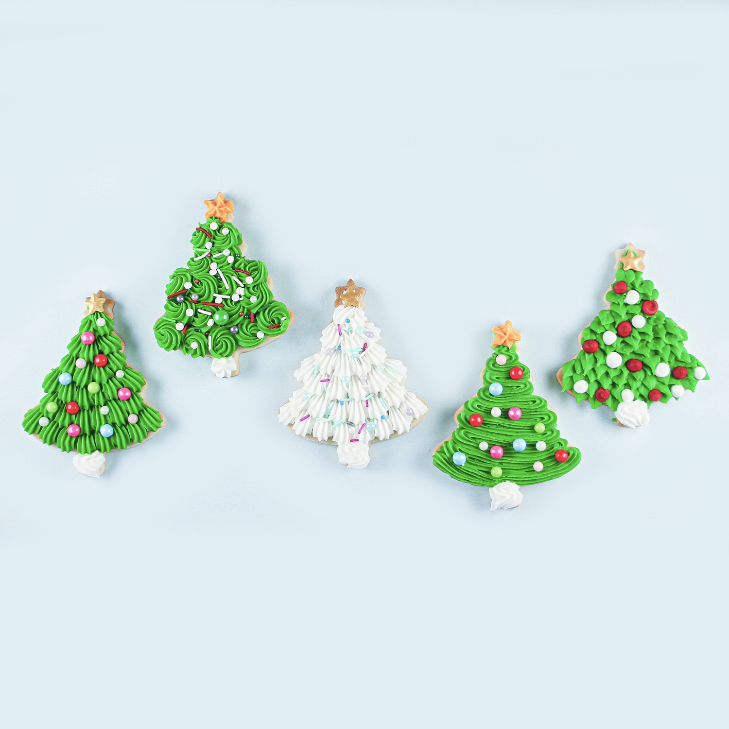 Christmas tree sugar cookies decoratd in buttercream using 4 different piping sytles with leaves, shells, rosettes and zigzags adorned with sprinkles and a star topping the trees.