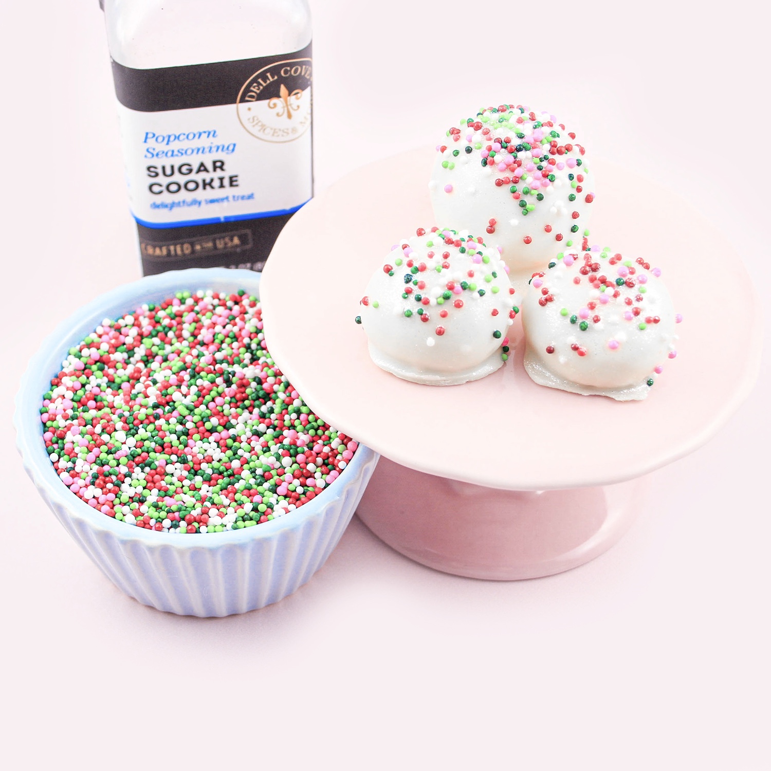 sugar cookie bon bons displayed on mini pink pedestral, sugar cookie popcorn seasoning and bright christmas non-pareils.