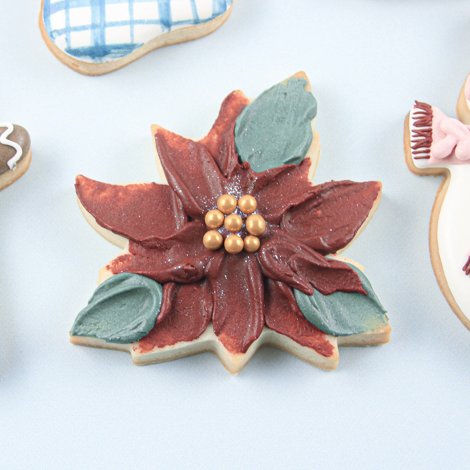 Poinsettia Royal Icing Cookie Decorated with a palette knife and adorned with gold sugar pearls.