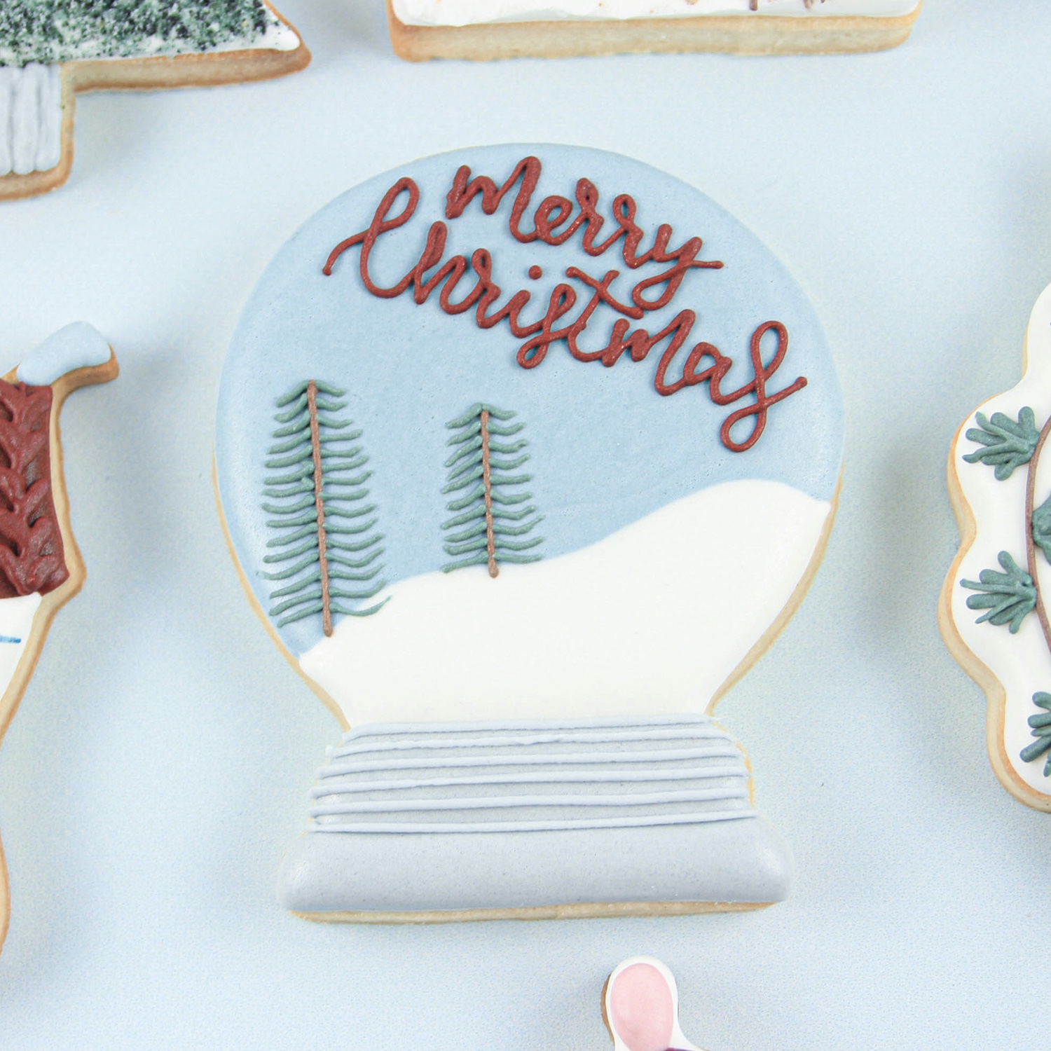 Snow Globe Cookie decorated with royal icing. Says Merry Christmas and has 2 pine trees