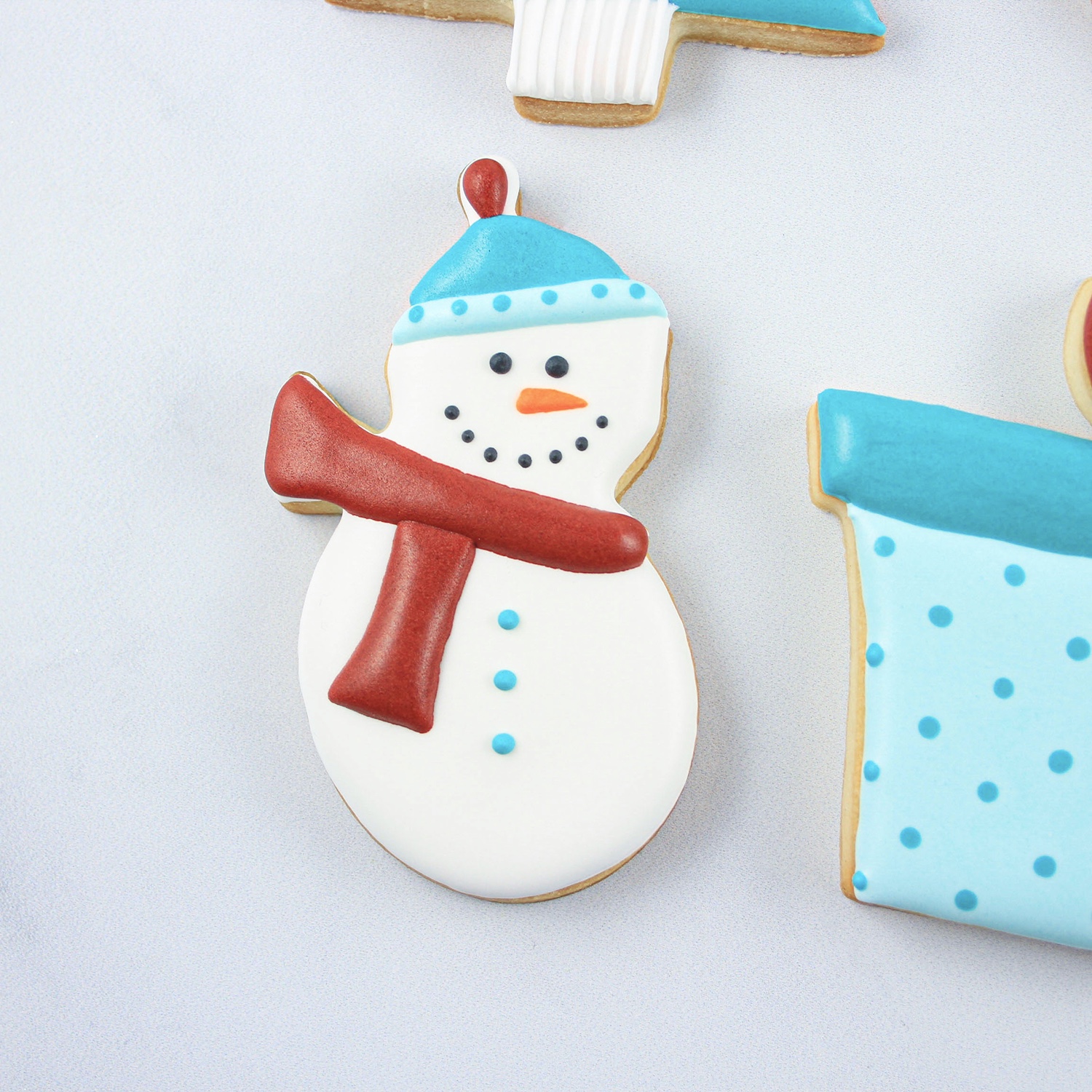 Snowman cookie decorated in royal icing with a red scarf and blue stocking cap