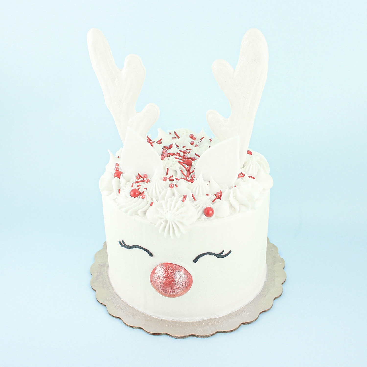 White Reindeer Cake with white buttercream swirls crown, chocolate red nose, white chocolate antlers and black buttercream eyelashes