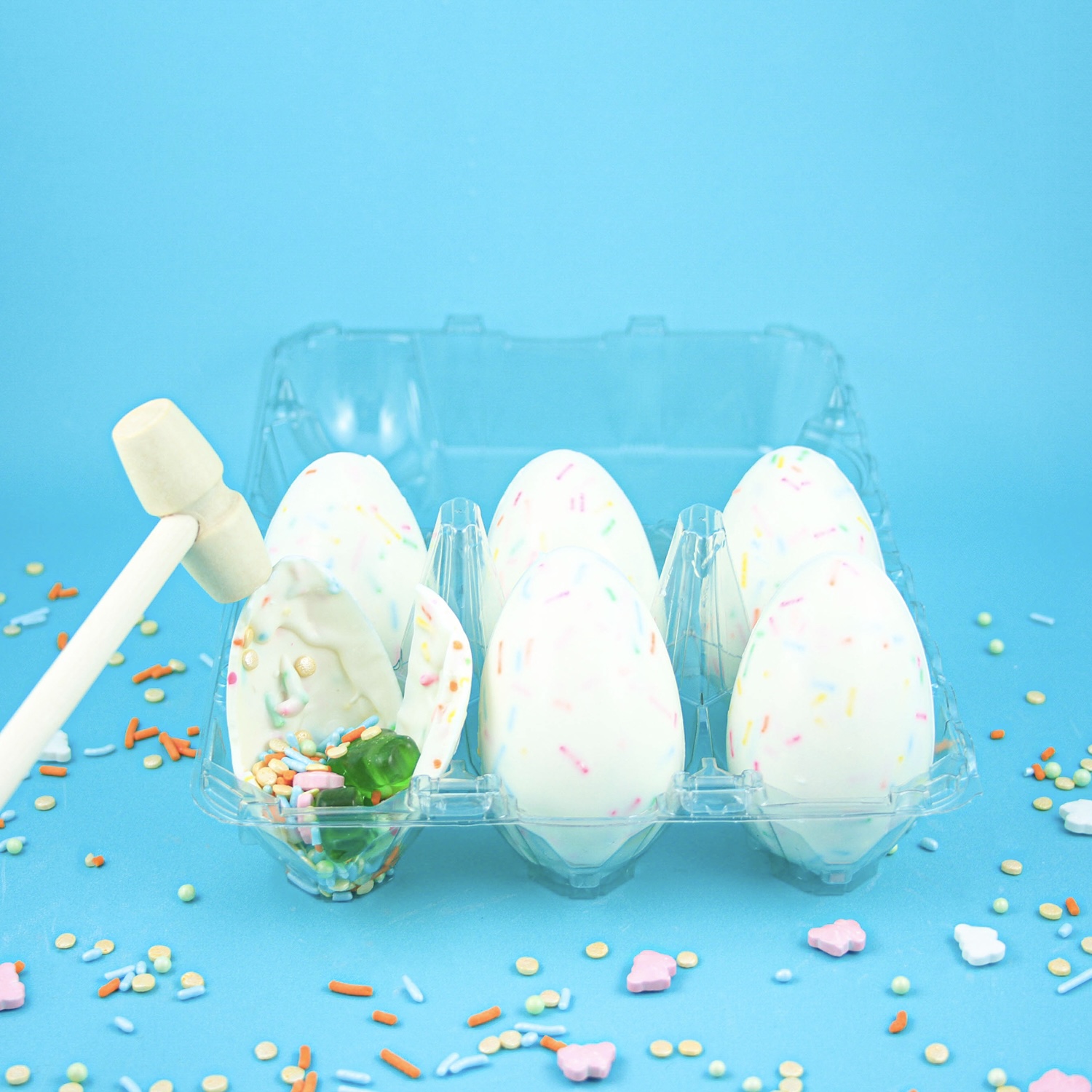 White chocolate breakable eggs in clear egg carton and a broken egg with gummy bears and sprinkles