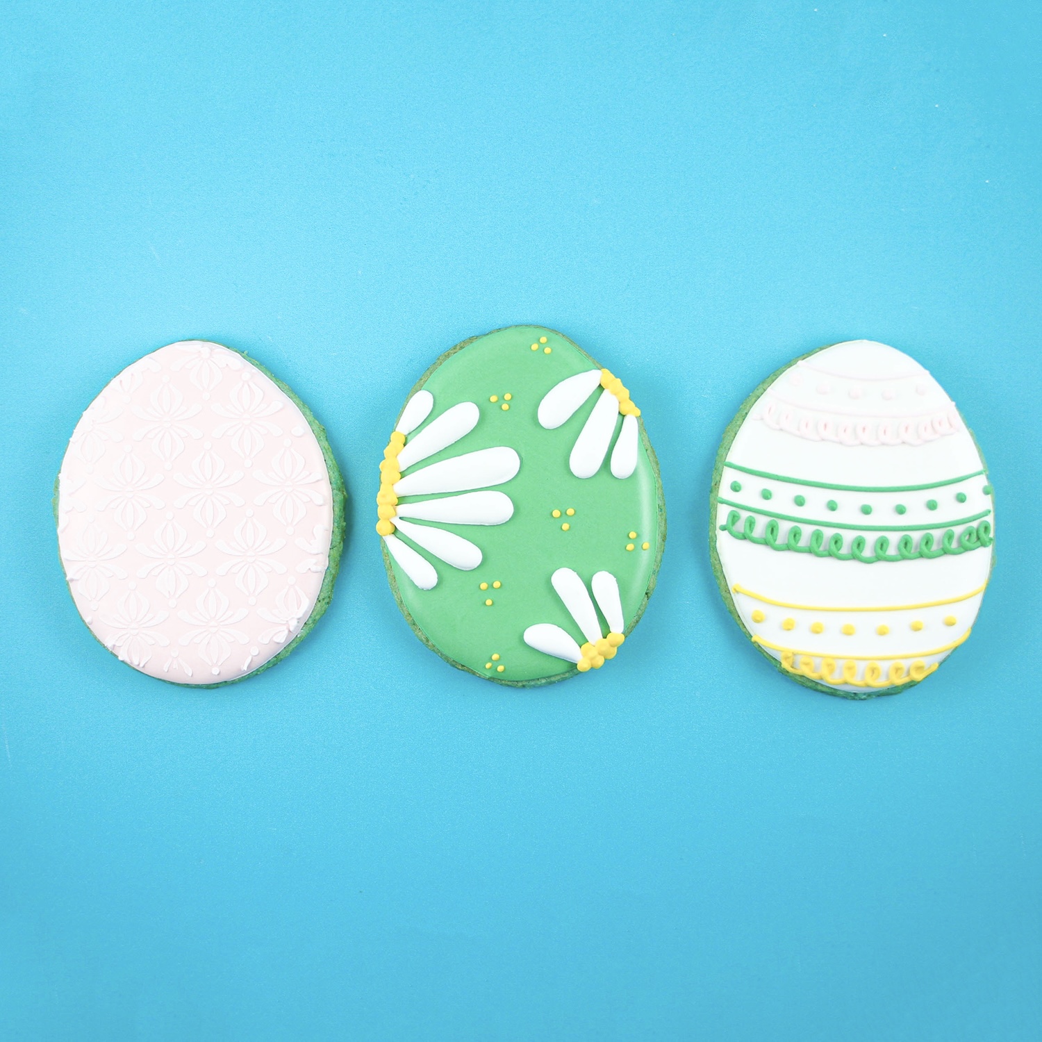 Three royal icing decorated easter eggs on blue sugar cookies