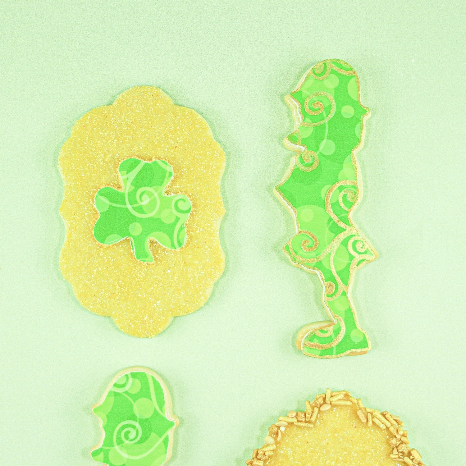 edible image cut shamrock in the middle of a plaque cookie, dipped in gold sanding sugar and a border of gold jimmies and sequins outline the cookie.