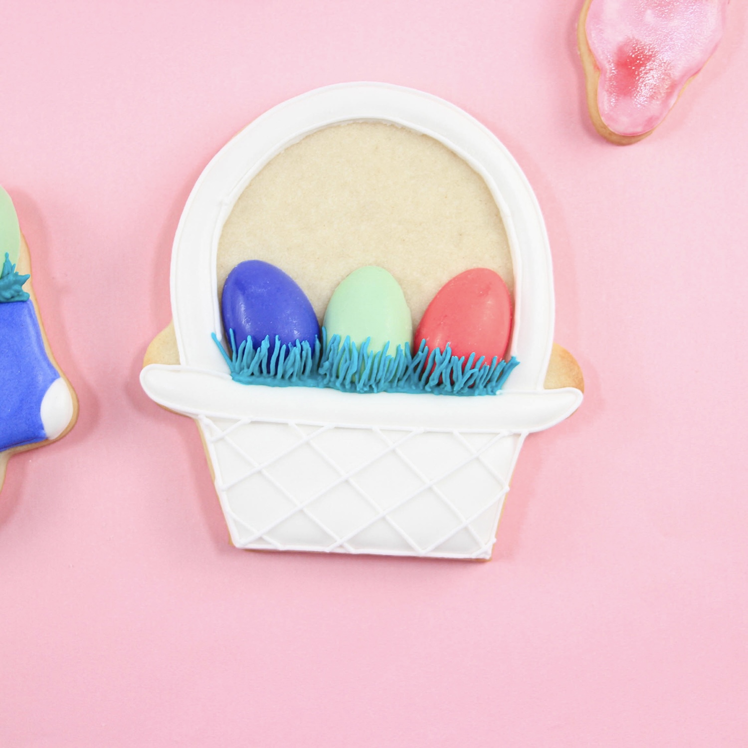 Royal icing white easter basket decorated cookie with colored candy coated eggs nestled in blue grass