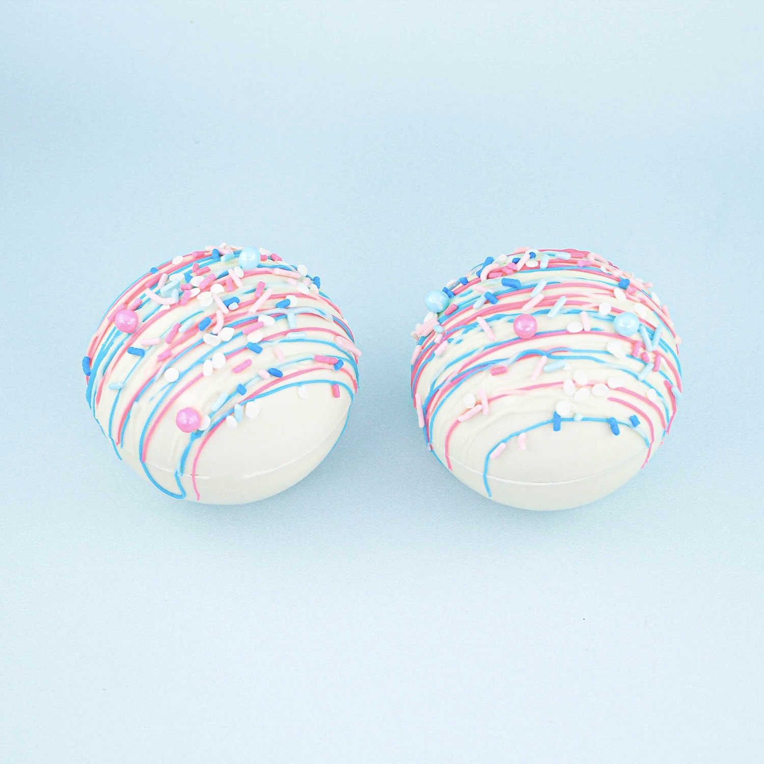 two completed white hot chocolate bombs with blue and pink accents for gender reveal