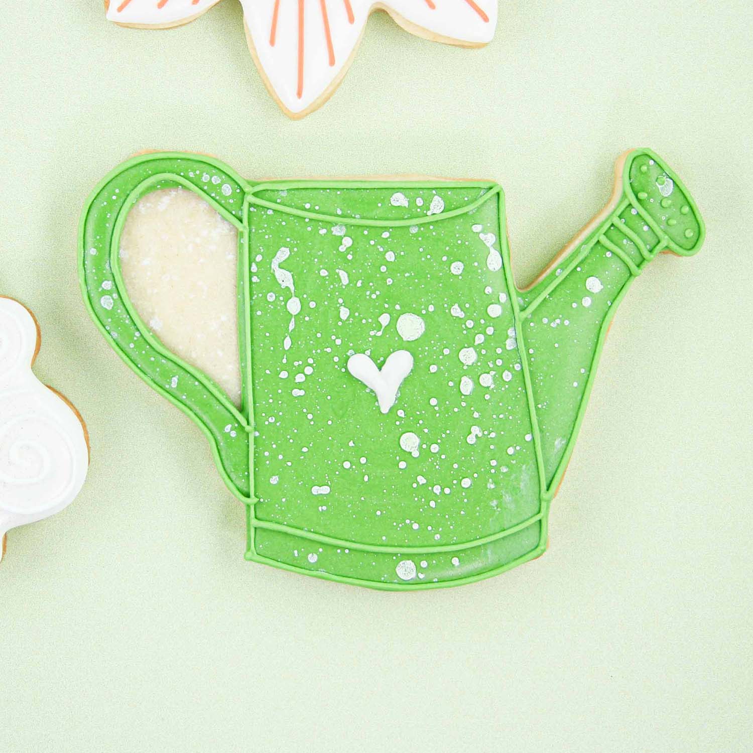 Watering Can cookie decorated in green royal icing, with a white spatter paint effect.