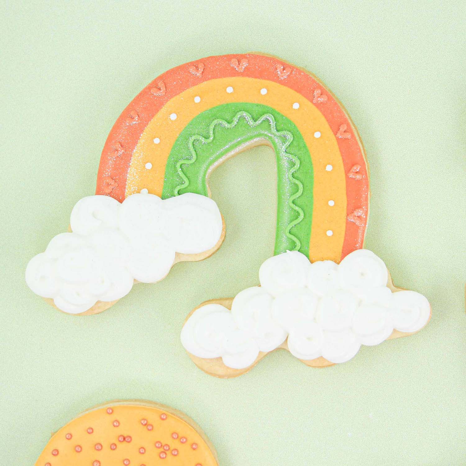 Rainbow Cookie with orang yellow and green arcs and fluffy white clouds decorated in royal icing