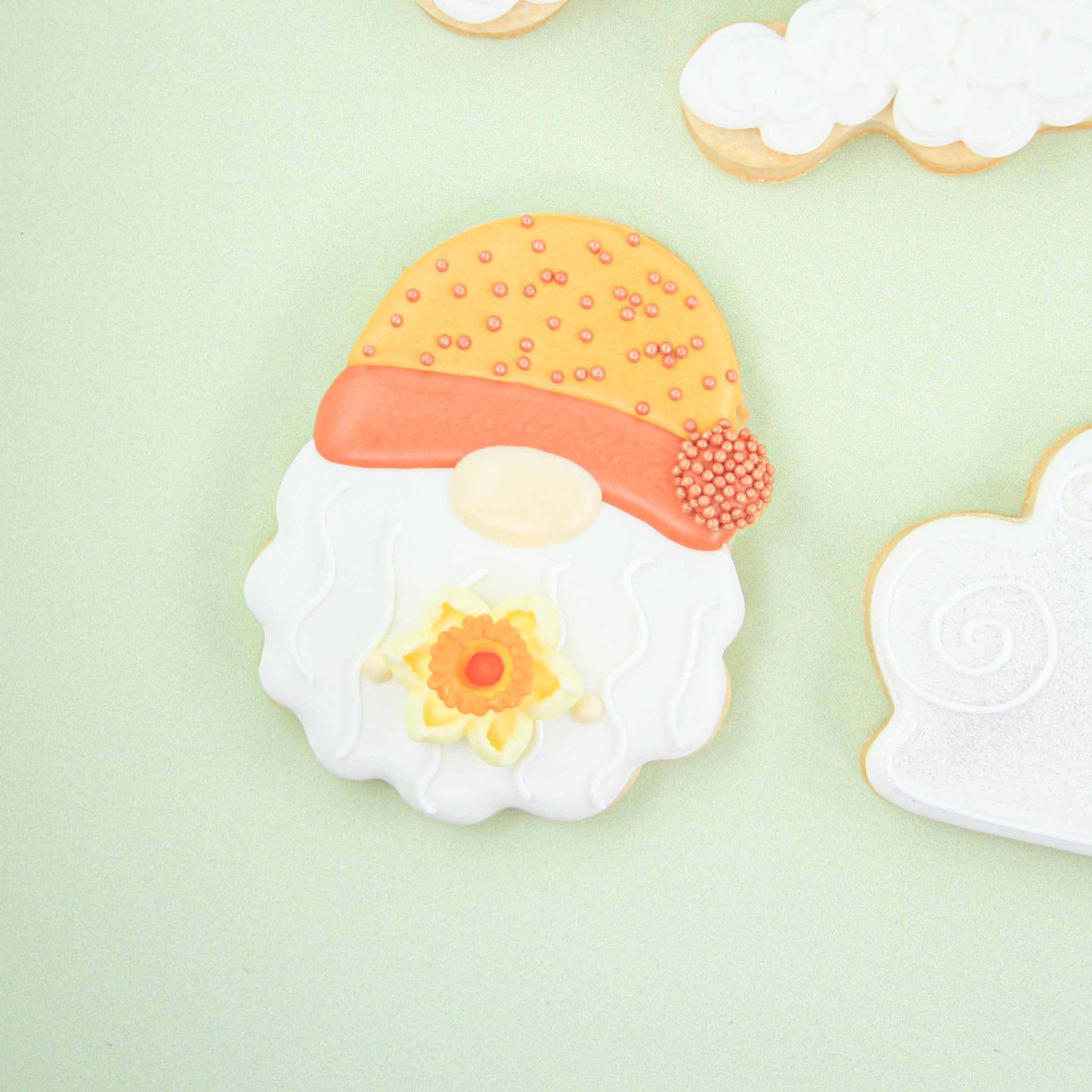 Gnome Cookie with a yellow and orange hat, whimsical white beard and a daffodil decorated in royal icing
