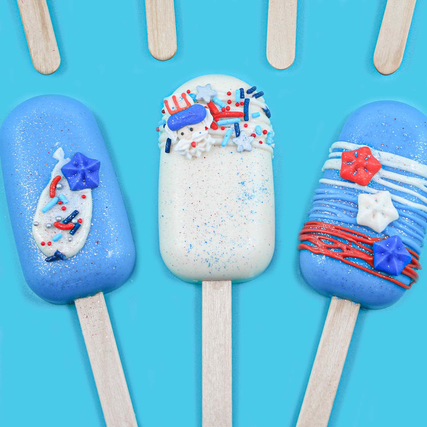 3 cakesicles in blue and white chocolate coating, drizzle, and decorated wiht jimmies, nonpareils, candy stars, patriotic sugar layons and jewel dust