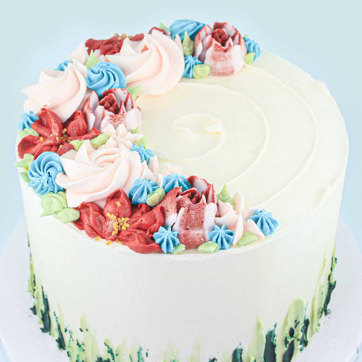 Pink, red, blue piped buttercream flowers in cresent shape on top of cake