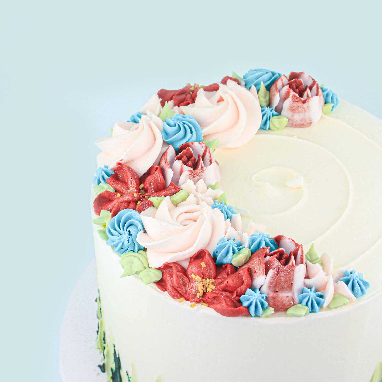Pink, red, and blue buttercream piped flowers in the form of a cresent on top of the cake.
