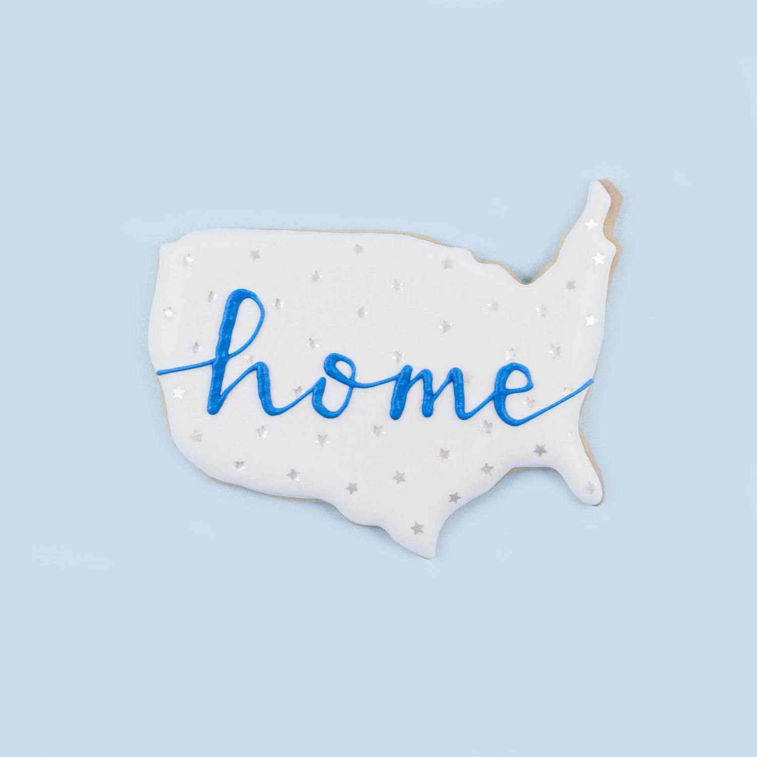 United state cut out cookie decorated in white royal icing, edible glitter stars and home lettering on the cookie