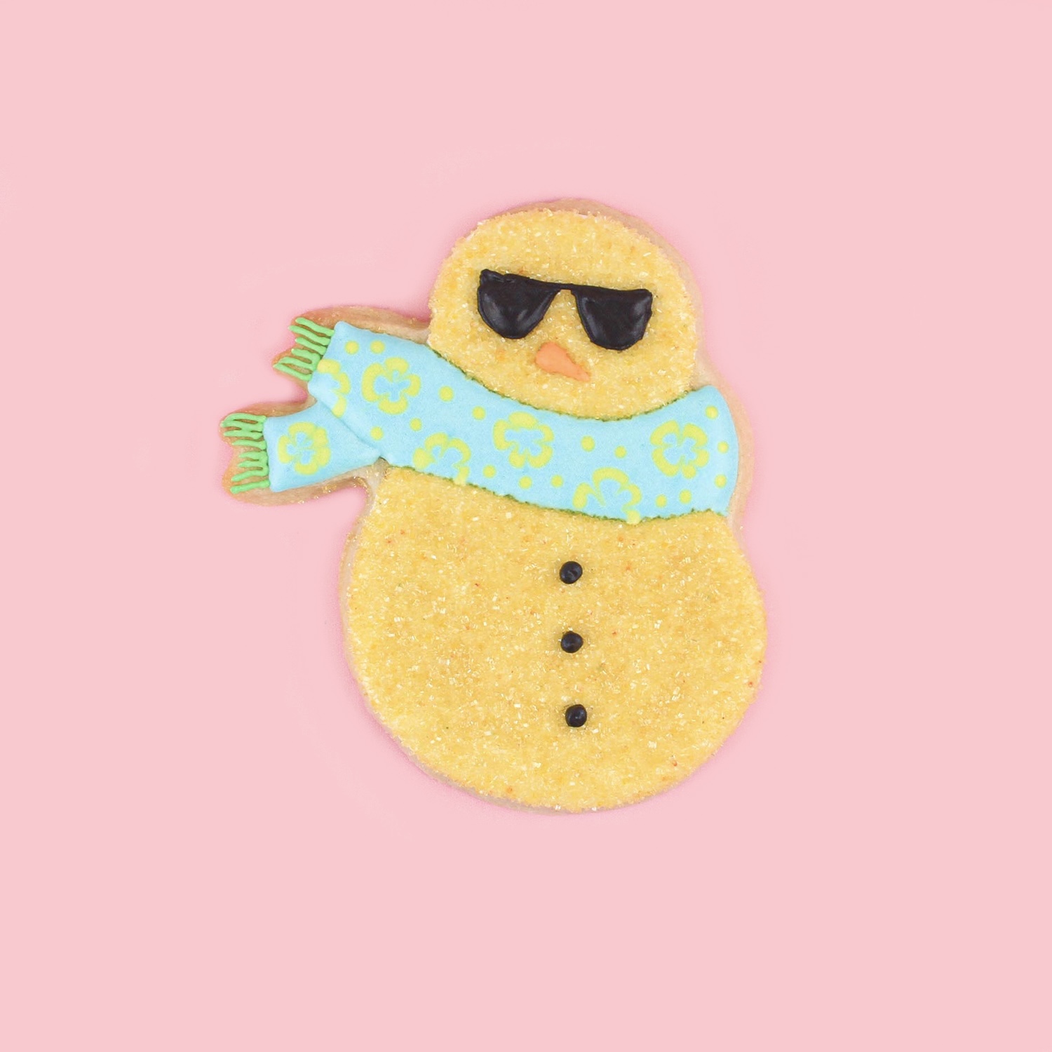 Snowman royal icng cookie dipped in gold sanding sugar and a blue royal icing scarf and sunglasses.