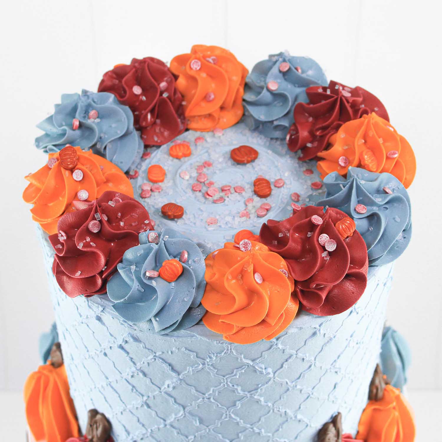 Swirls in burgundy, wedgewood and pumpkin buttercream piped with a 1M tip and sprinkles of red confetti, blue sugar crystals and edible pumpkin sprinkles.