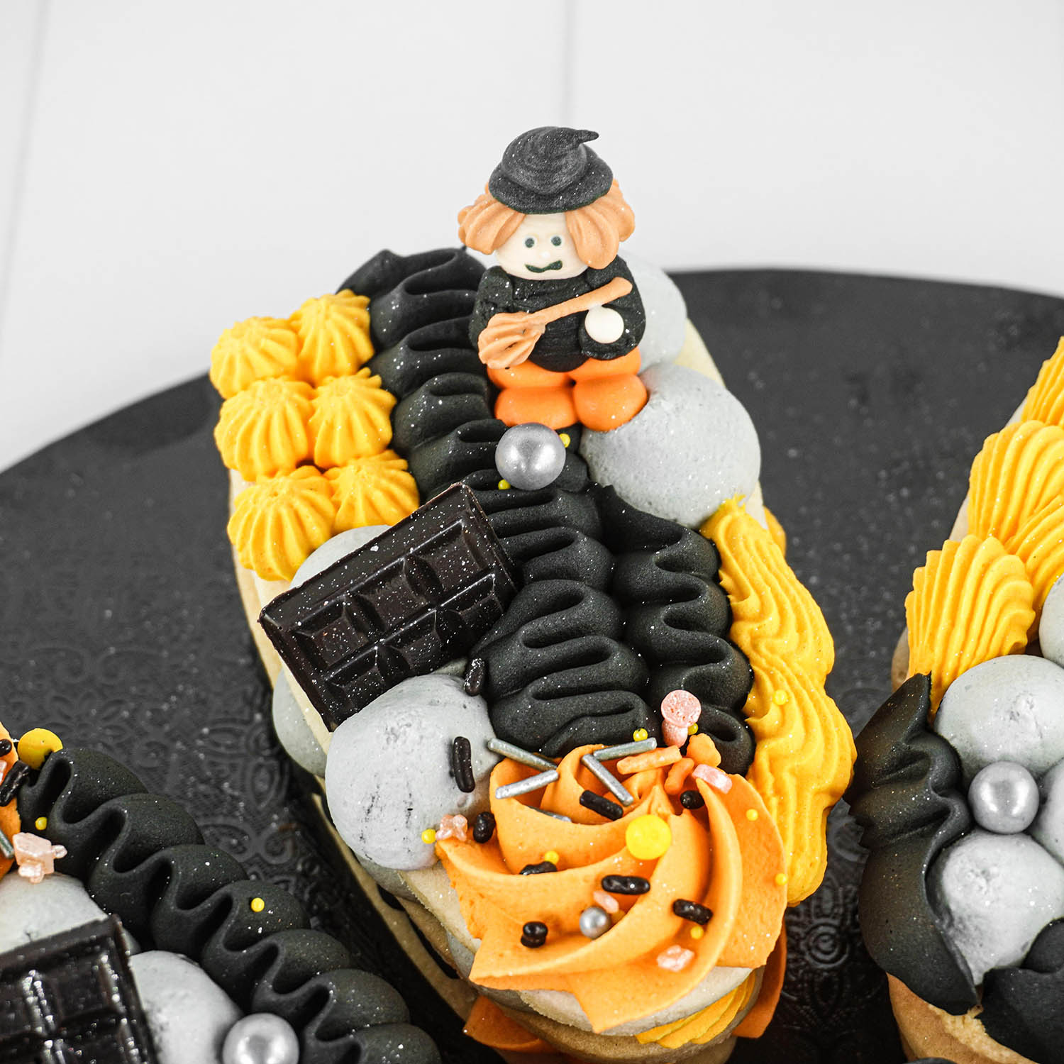 3 layer buttercream cookie with yellow, pumpkin, slate and black piped buttercream with a chocolate bar and witch sugar layon.