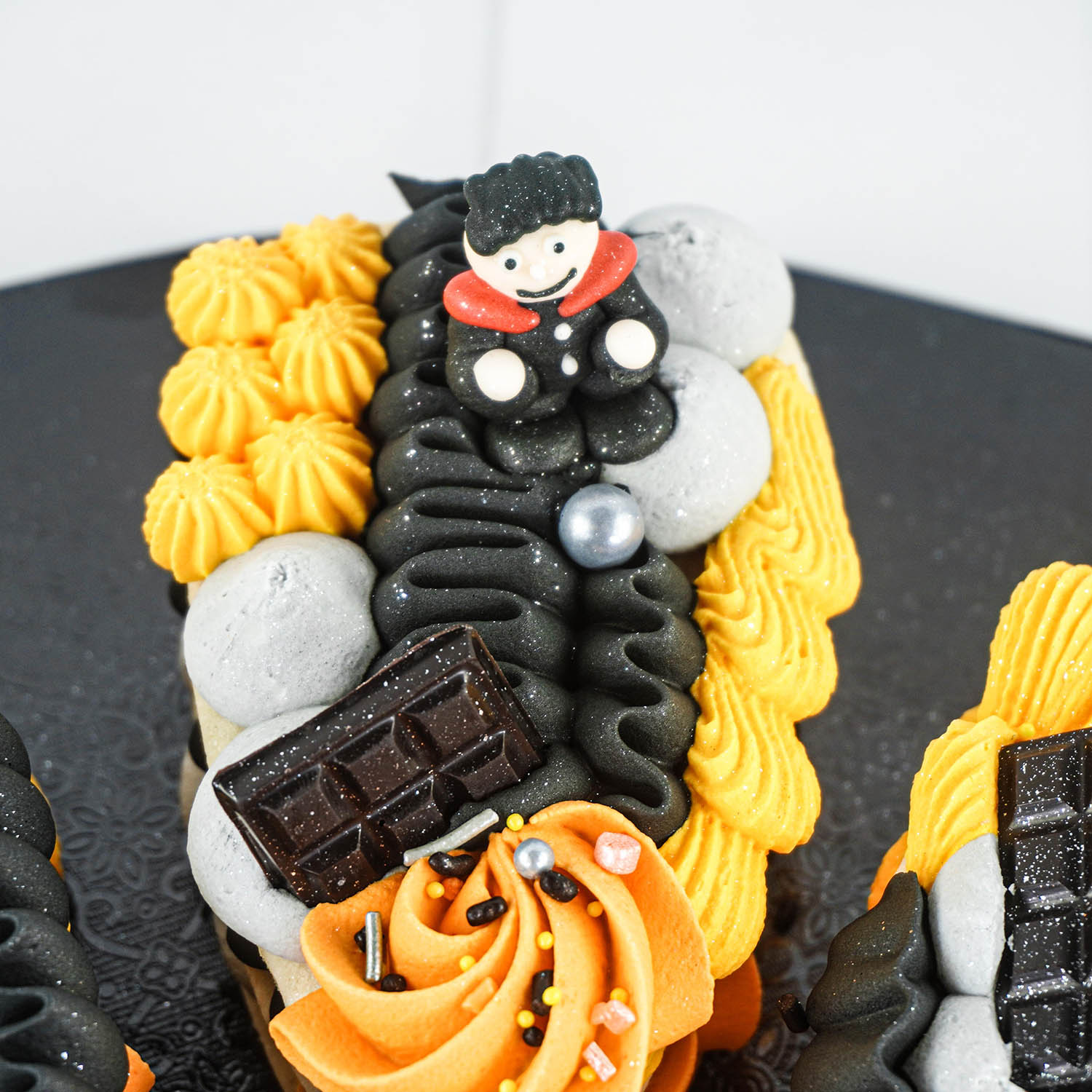 3 layered buttercream cookie with yellow, pumpkin, slate and black piped buttercream in rosettes, squiggles and dots. deocrated with sprinkles and vampire sugar layon.