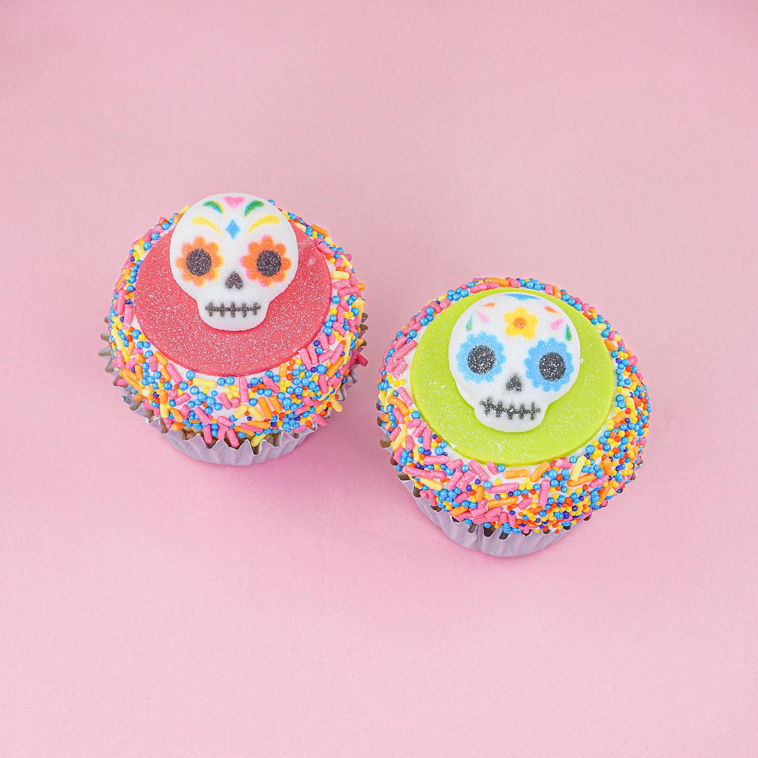 Day of the Dead pinkl fondant and sprinkle cupcake and a green fondant sprinkle cupcake with skull sugar layons