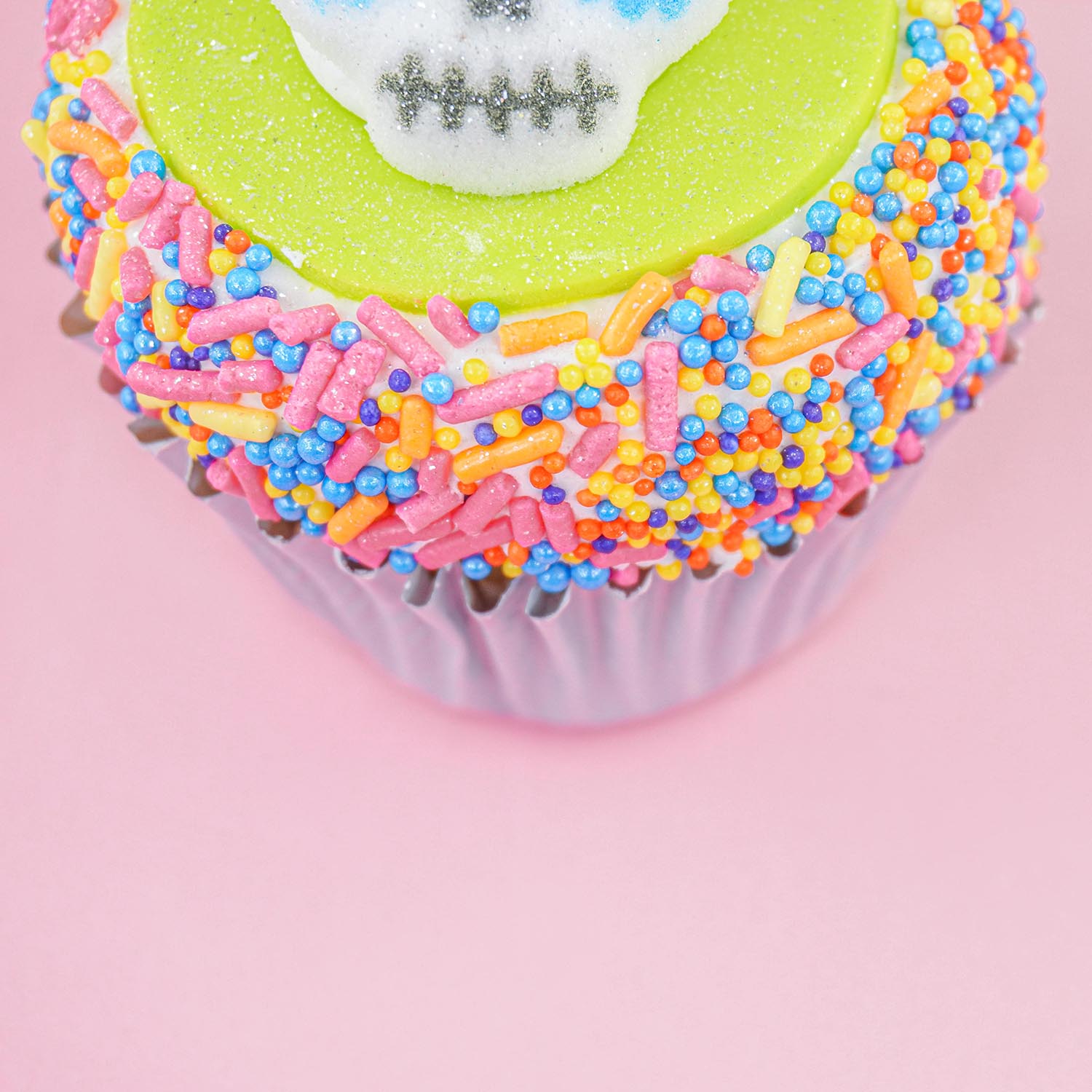 Green fondant and sprinkle cupcake with sugar skull layon