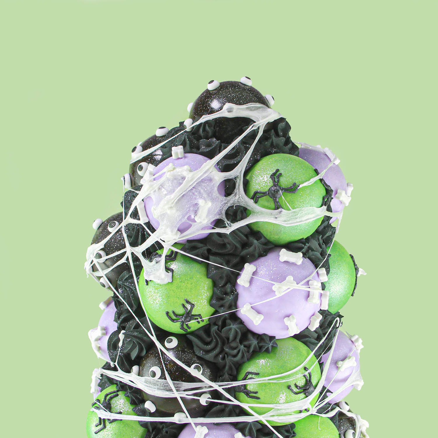 Top of the Cake pop tower with black cake balls with beady eyes, green cake balls with hand piped spiders and purple cake balls with candy bones covered under a marshmallow web.