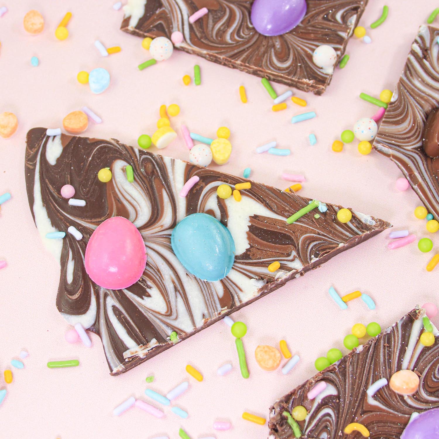Finished Piece of Easter Bunny Chocolate Bark showing dark, milk and white chocolate swirls and pieces adorned with chocolate molded bunnies, colored chocolate jelly bean eggs and a sprintime colored sprinkle mix that glitters
