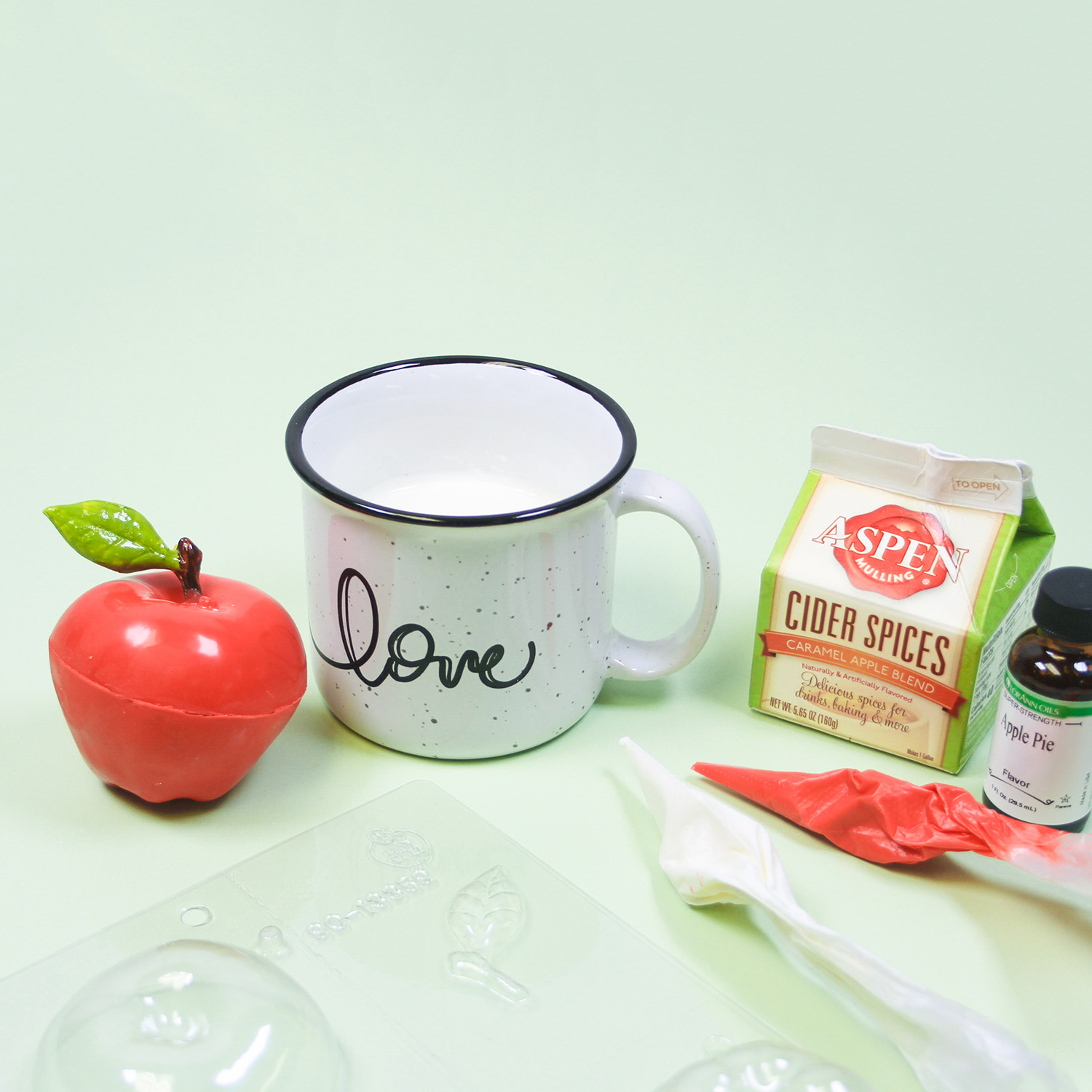 Apple Cider bomb with the mold and candy coating and ingredients on display with a mug of hot milk