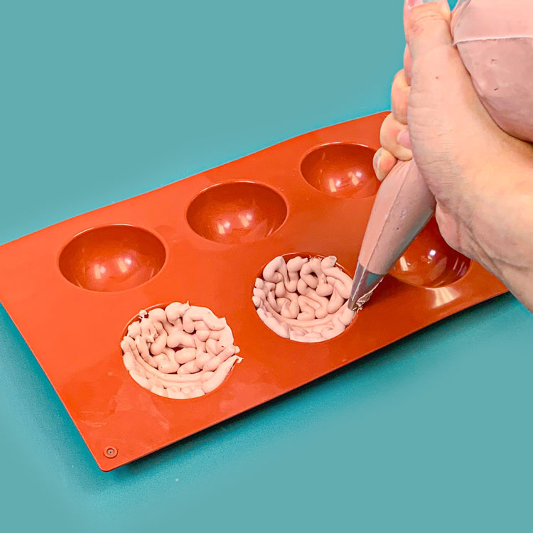 piping buttercream into hemisphere mold in brain pattern