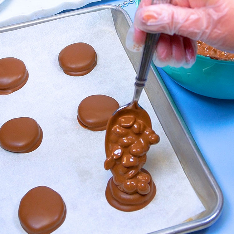 spooning peanut chocolate mixture onto chocolate covered patty
