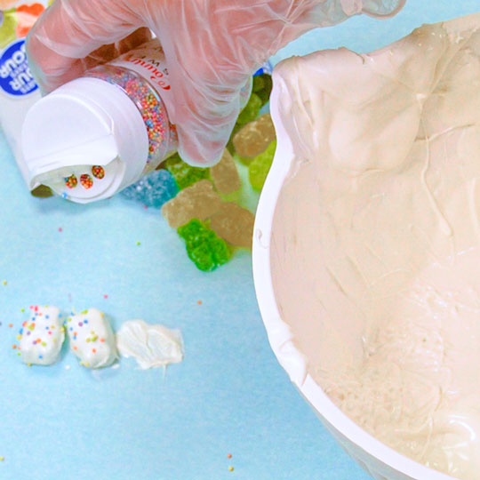 adding rainbow sprinkles to chocolate dipped gummy bear