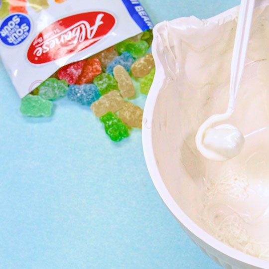 using dipping tool to cover gummy bear in melted chocolate