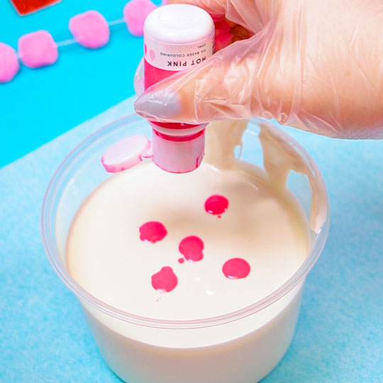 adding hot pink colour mill to melted white chocolate