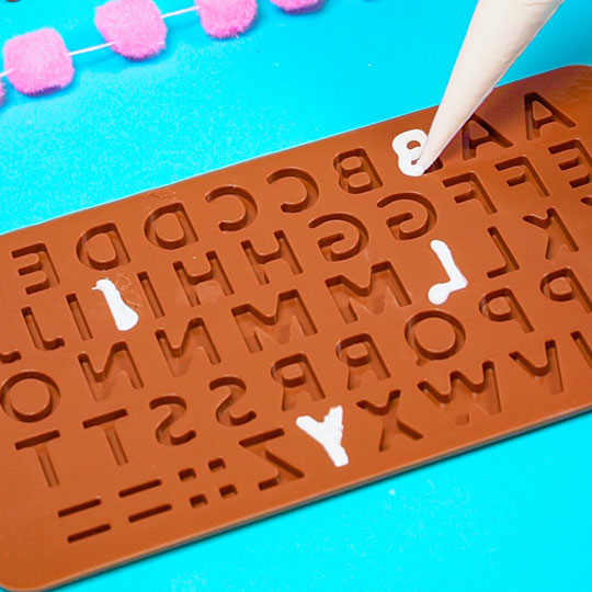 piping melted white chocolate into letter mold