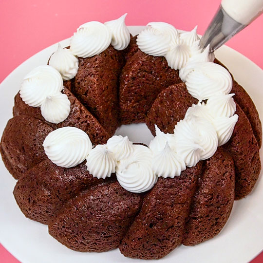 piping buttercream onto a chocolate bundt cake