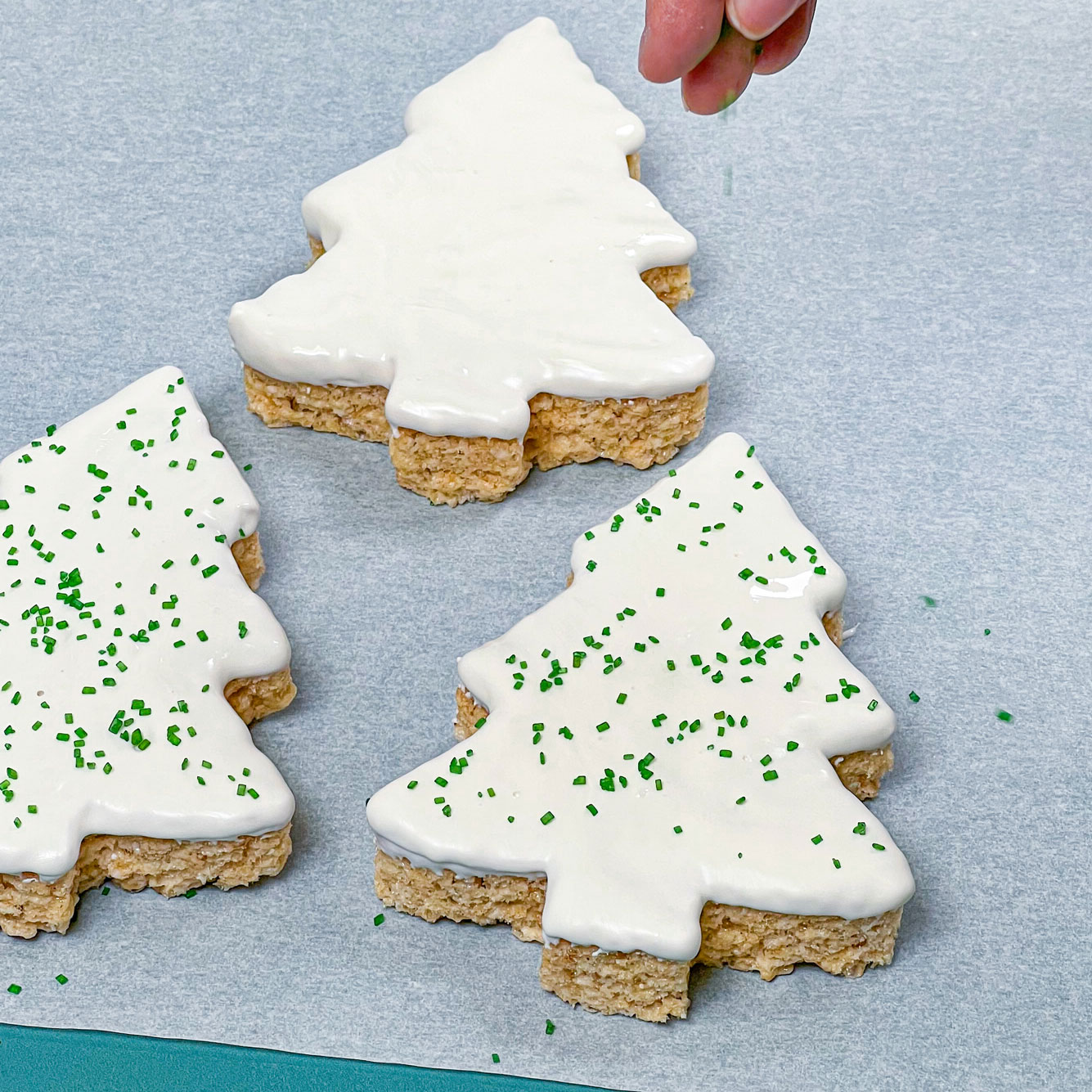 adding green sprinkles to white chocolate christmas tree rice krispie treats