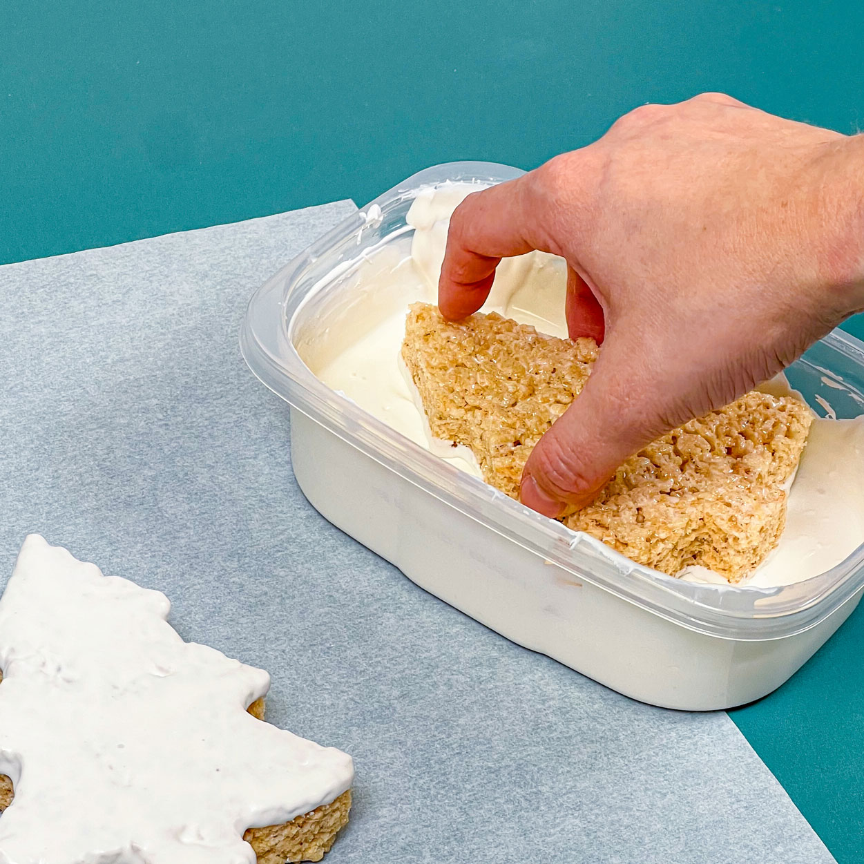 dipping christmas tree rice krispie treat into melted white chocolate