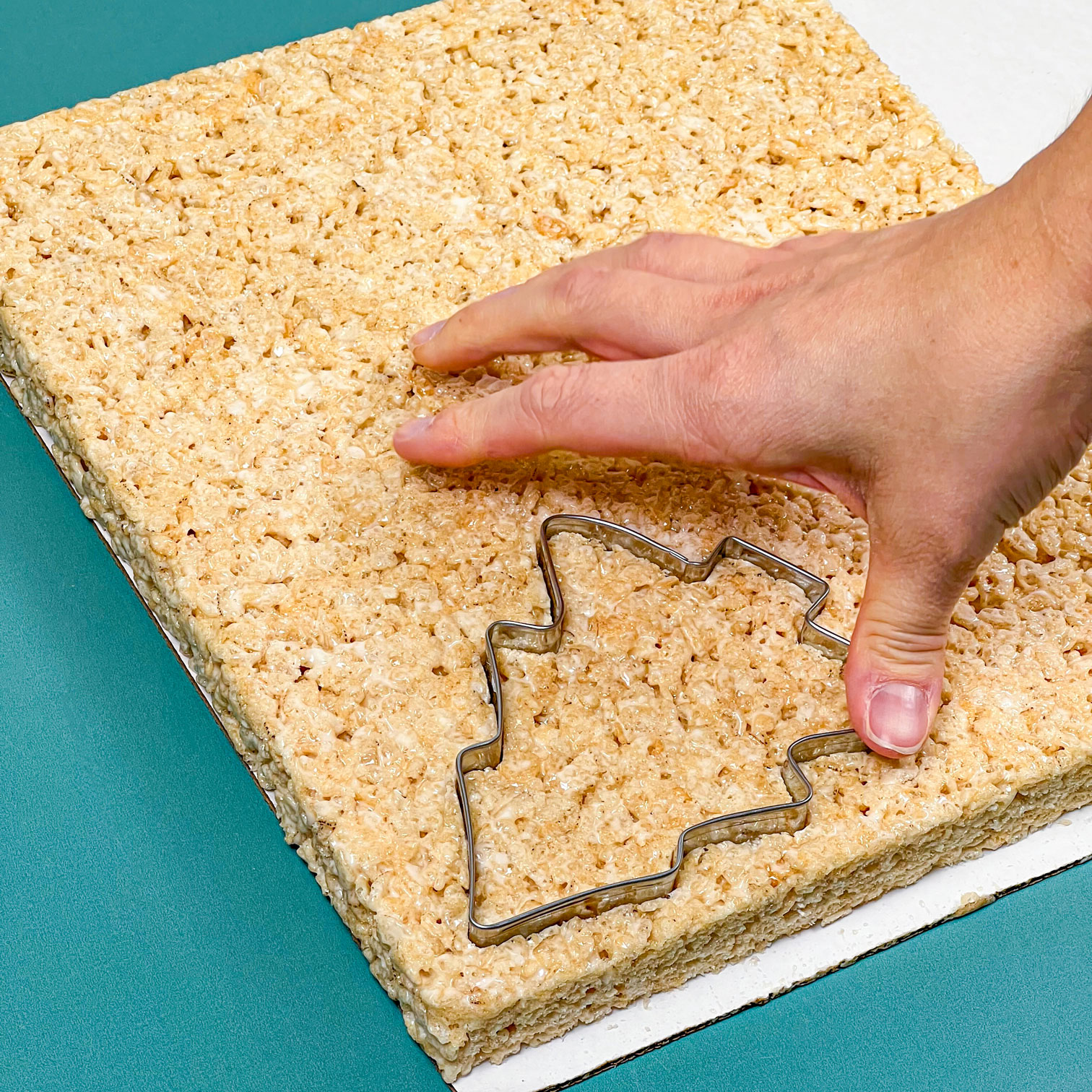 using a cookie cutter to cut out rice krispie treat christmas trees