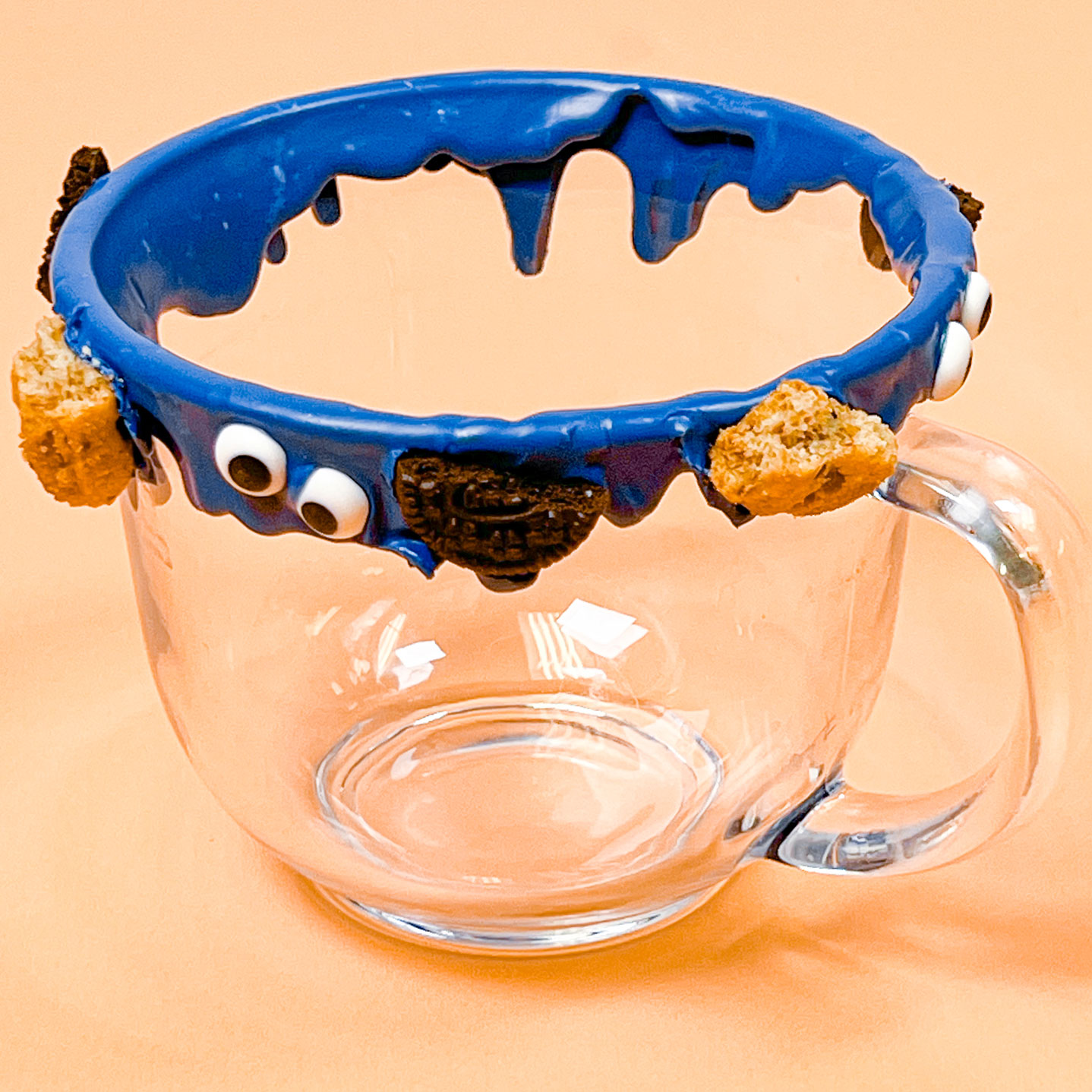mug with blue chocolate drip decorated with icing eyes and cookie pieces